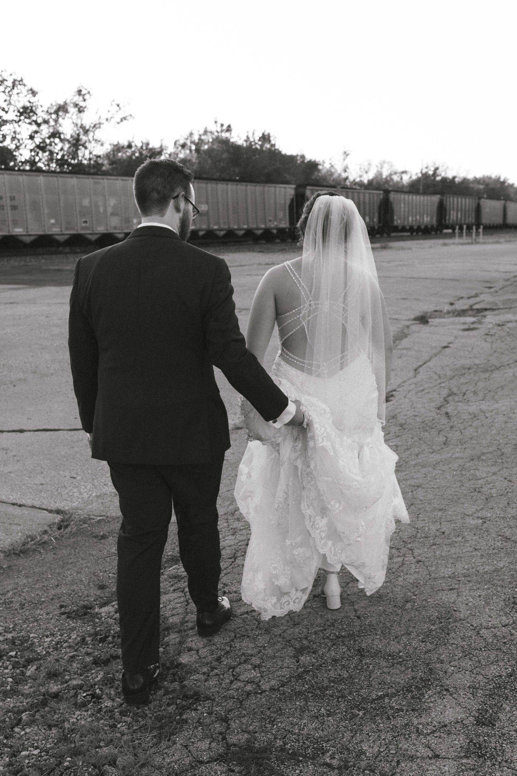 Black and white candid moment of bride and groom walking alongside train at venue in Missouri