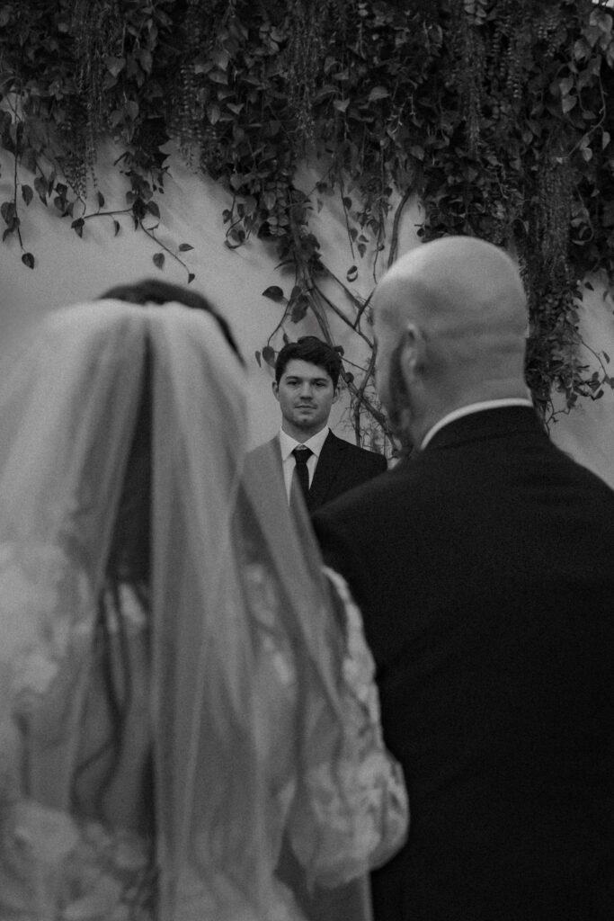 Wide shot of bride walking down the aisle with her father, groom visible waiting at the altar.