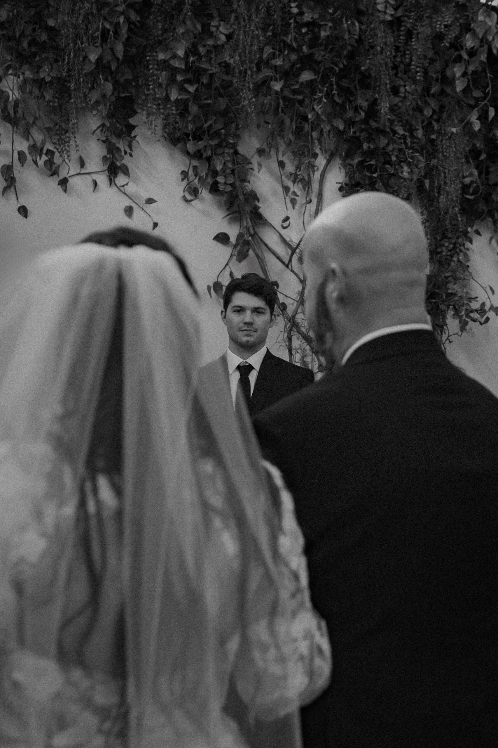Wide shot of bride walking down the aisle with her father, groom visible waiting at the altar.