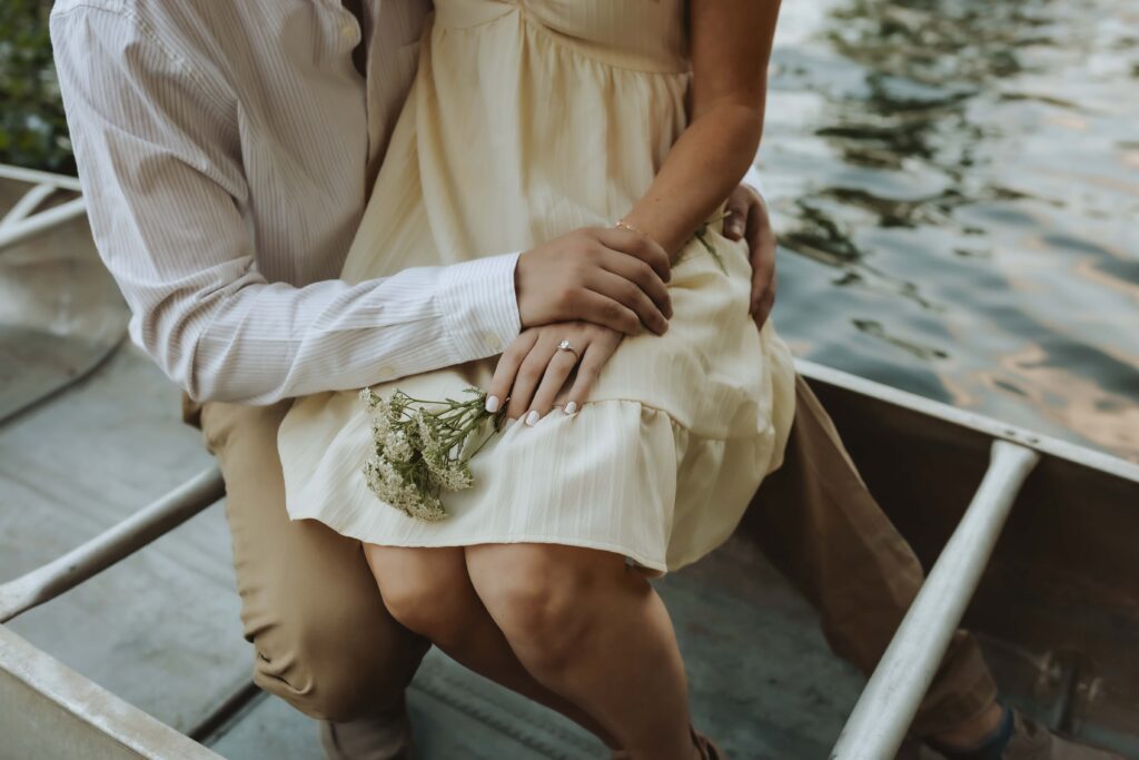 Couple enjoying a romantic canoe ride on a calm lake at sunset, holding hands and smiling, surrounded by golden reflections and peaceful nature.