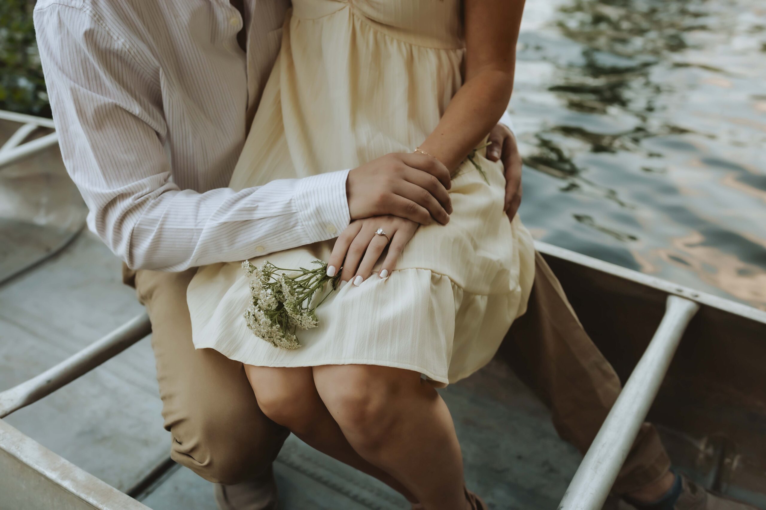 Couple enjoying a romantic canoe ride on a calm lake at sunset, holding hands and smiling, surrounded by golden reflections and peaceful nature.