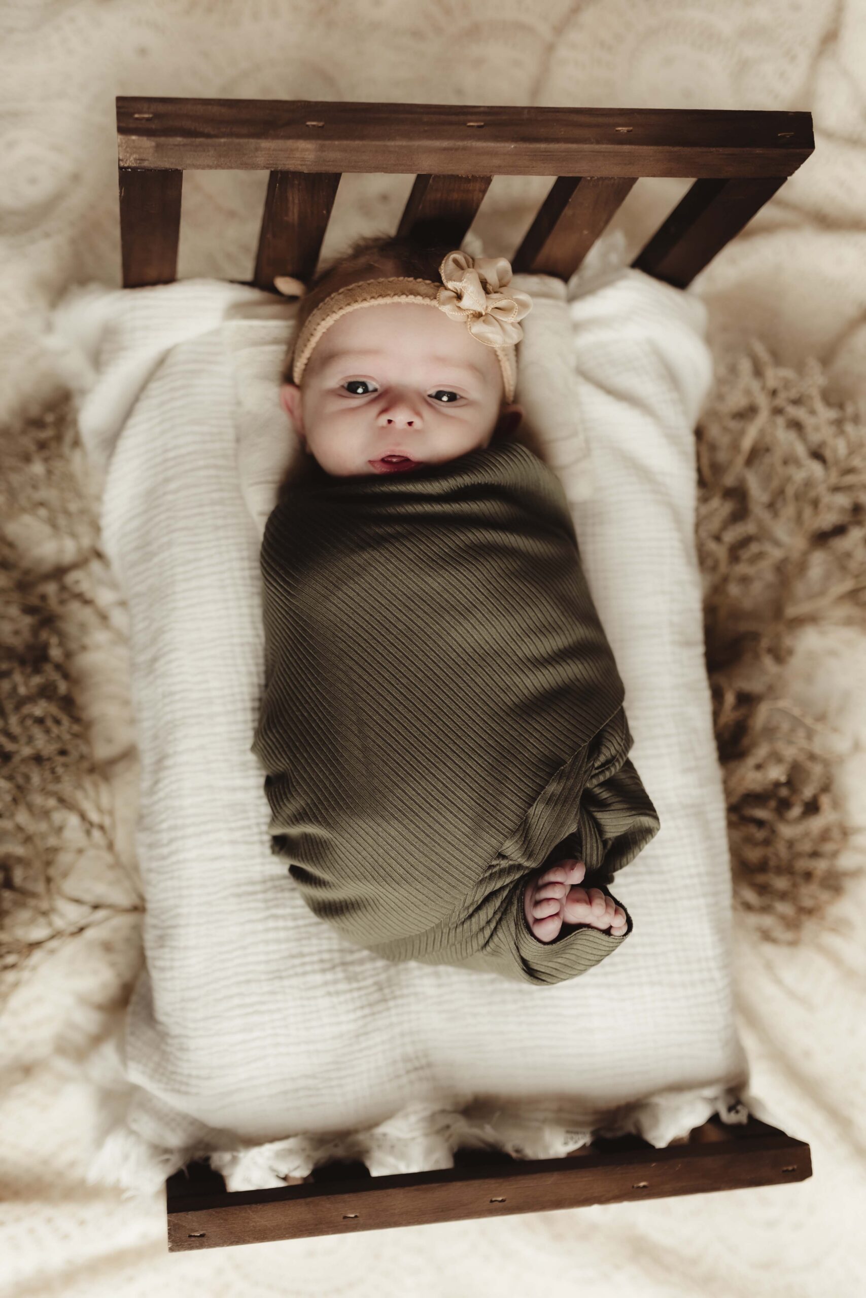 Swaddled newborn posed on a tiny boho-style crib with soft textured blankets