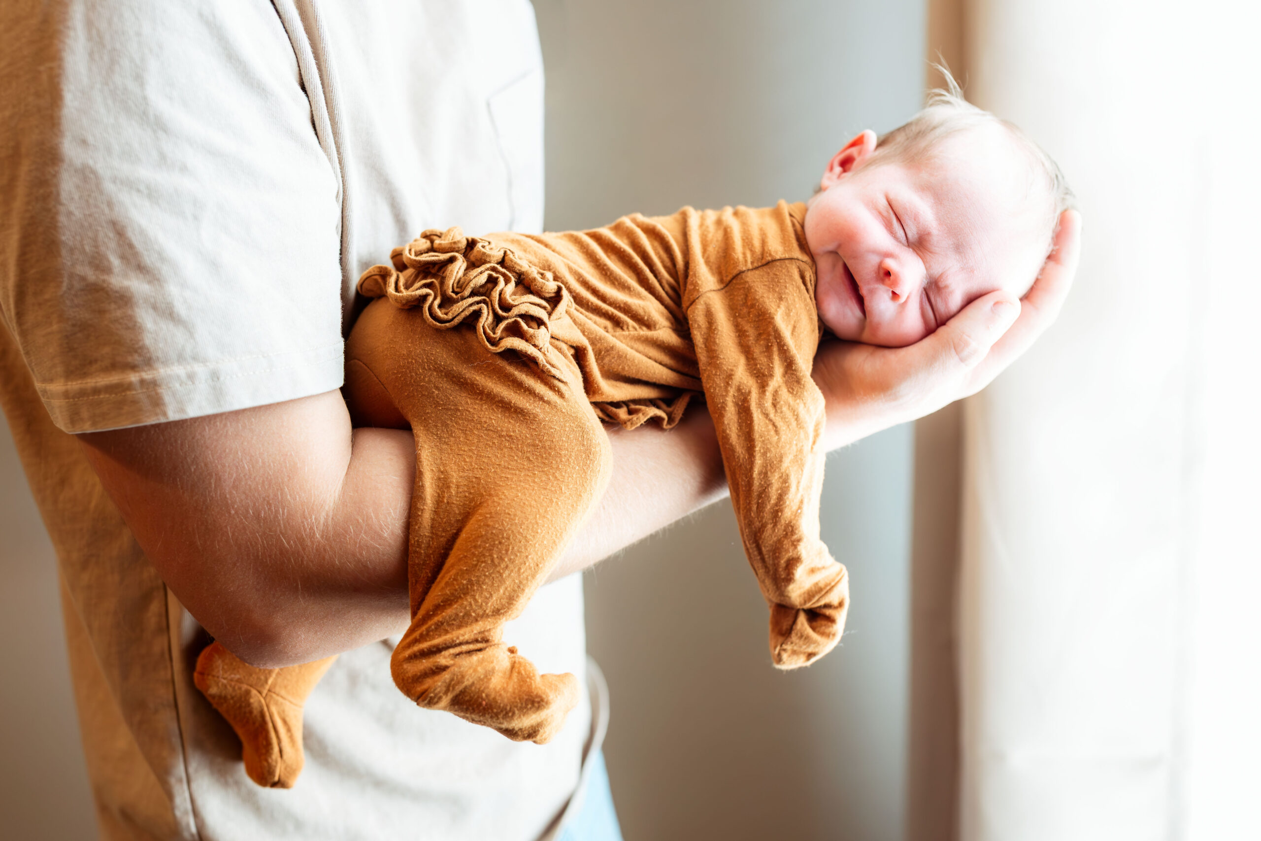 Newborn baby smiling while being gently cradled in father’s arms during an in-home lifestyle photography session.