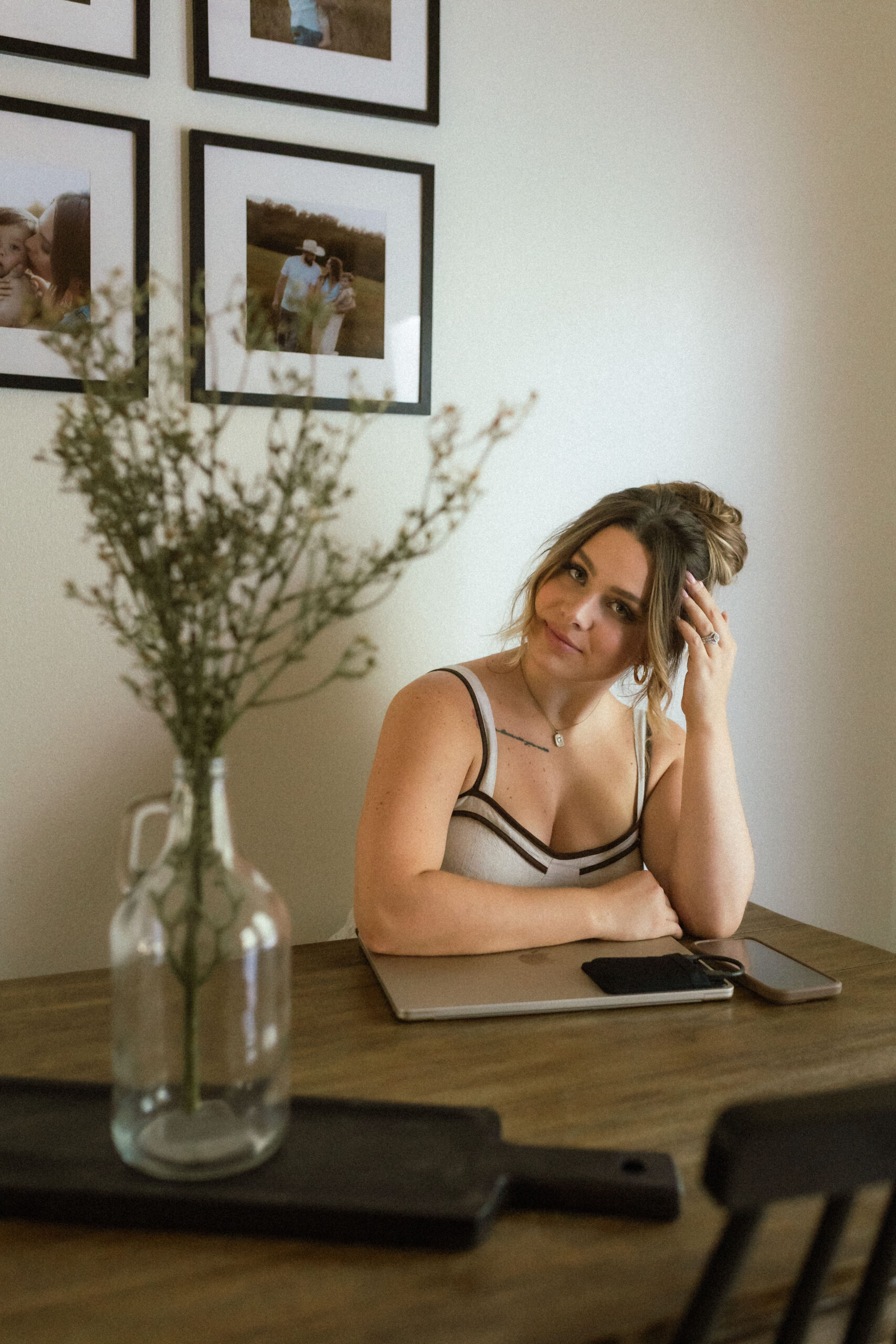 Earthy, neutral-toned headshot of a wedding and family photographer seated at her work table with a laptop and phone, captured in soft January light