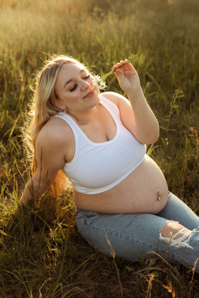 Outdoor maternity photo in Missouri showing pregnant woman in casual jeans and cropped top highlighting baby bump in natural golden light.