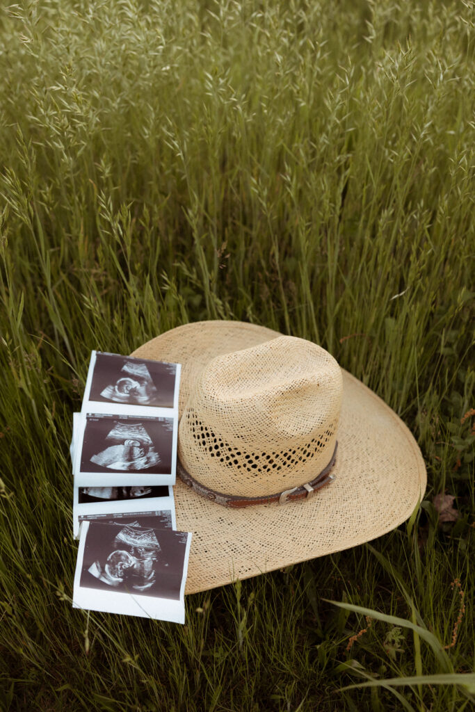 Outdoor maternity detail photo in Missouri showing cowboy hat and ultrasound prints celebrating baby in natural golden light.